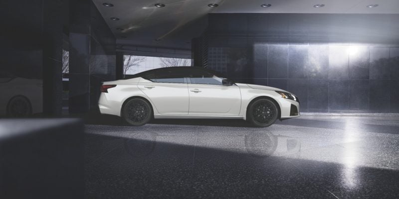 White 2026 Nissan Altima sedan shown in side profile, parked in a dark garage with dramatic overhead lighting