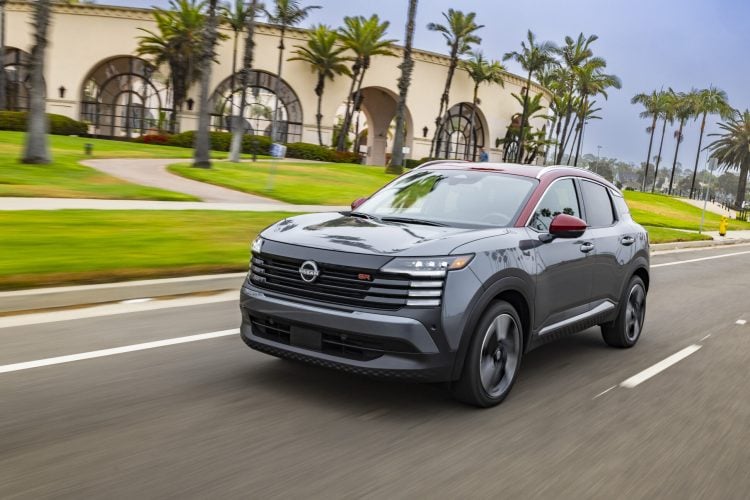 2026 Nissan Kicks SR in two-tone gray and red paint accelerating down a palm tree-lined street past a resort-style building.