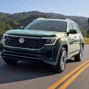 Green Volkswagen Atlas SUV driving on a two-lane road with mountains in the background for a Volkswagen Atlas Review.