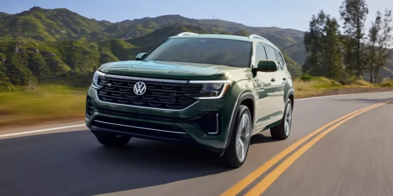 Green Volkswagen Atlas SUV driving on a two-lane road with mountains in the background for a Volkswagen Atlas Review.