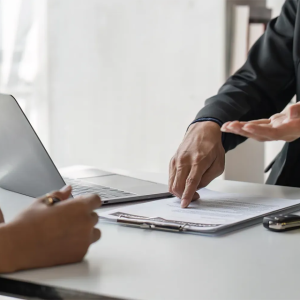 Customer and car dealer discussing invoice price details with contract and toy cars on a desk
