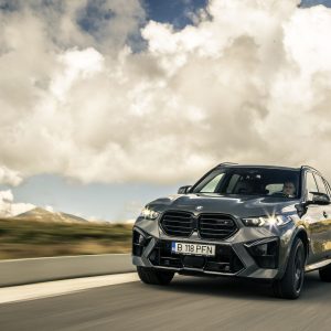 A BMW X5 driving on a desert road at sunset with lens flare, featured in our BMW X5 Review.