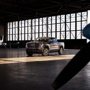 Gray 2026 GMC Sierra 1500 pickup truck parked inside an airplane hangar with a private jet and propeller in the background