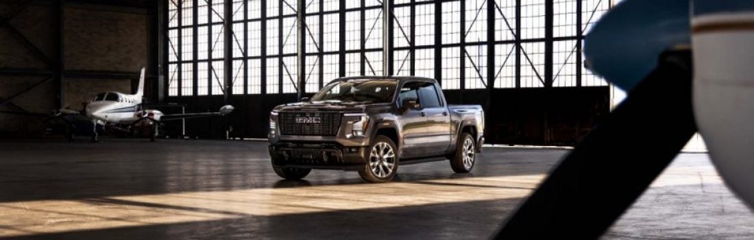 Gray 2026 GMC Sierra 1500 pickup truck parked inside an airplane hangar with a private jet and propeller in the background