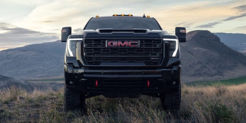 2025 GMC Sierra HD AT4X in Onyx Black facing forward on a hilltop with mountain range and dramatic sky in the background
