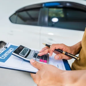 Buyer reviewing a car purchase contract and calculator during a dealership price negotiation
