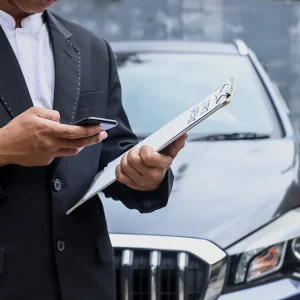 Car buyer checking invoice price information on a clipboard and phone before purchasing a vehicle