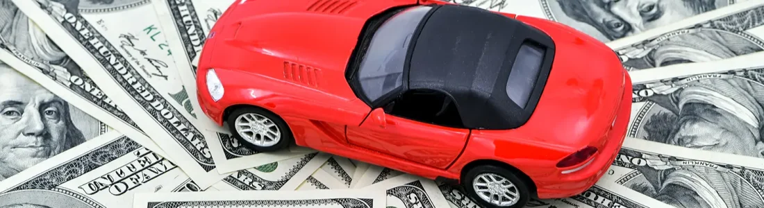Red toy car on hundred dollar bills representing costly invoice car price lookup mistakes