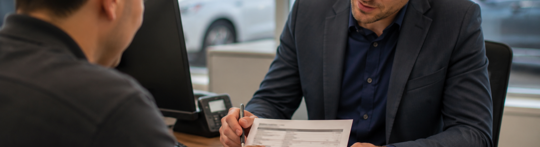 Two professionals review a printed form together at a desk in a bright office, one holding a pen over the document.